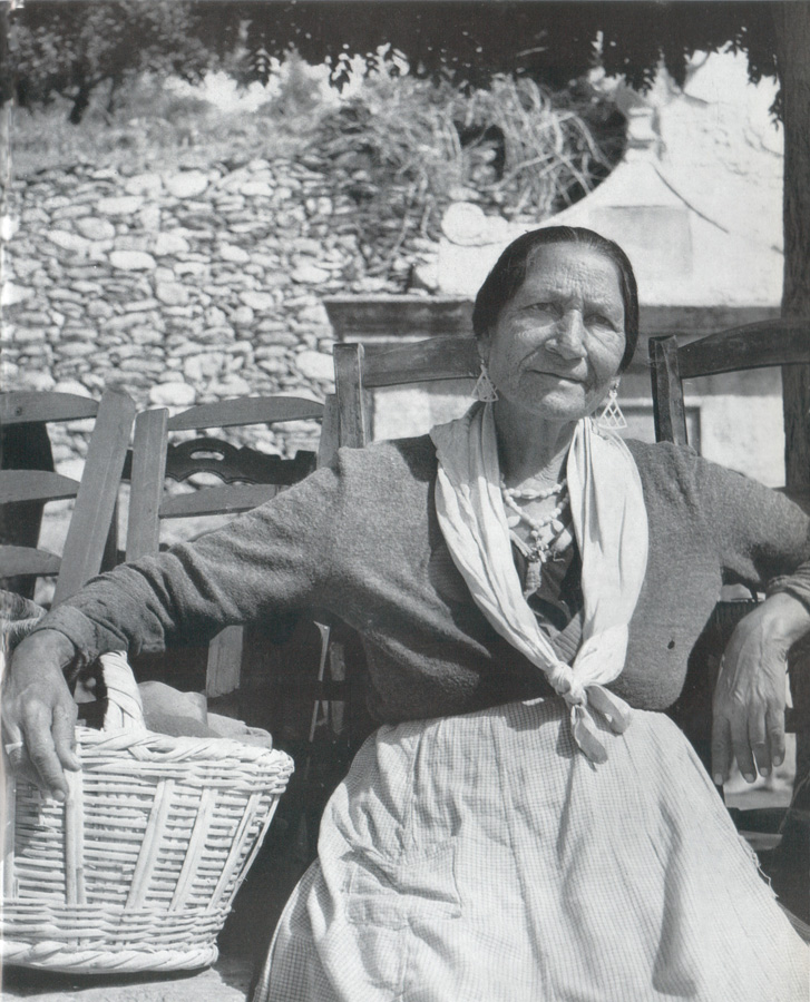 Retrato de una mujer gitana sentada con un cesto de mimbre, pendientes y pañuelo, en un exterior soleado